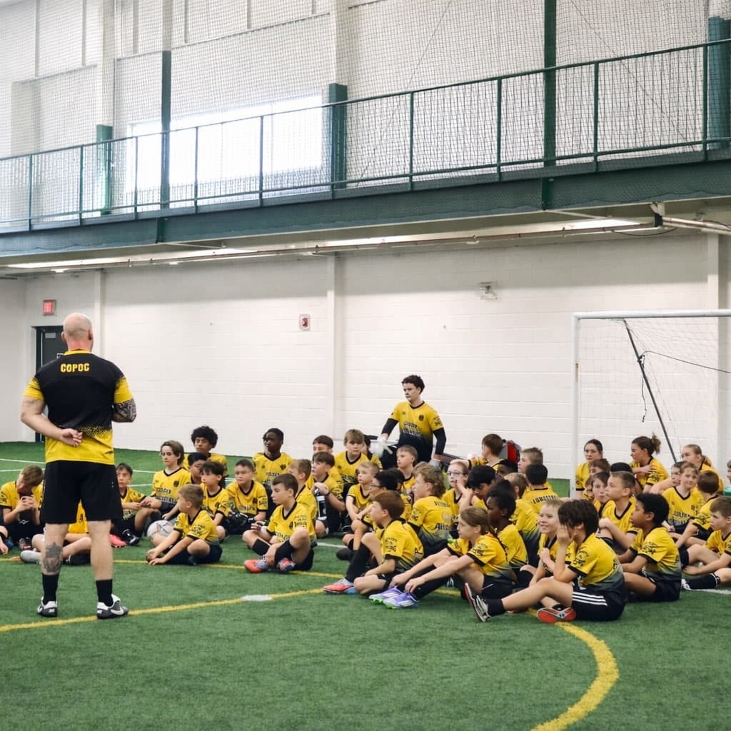 Coach addressing a seated group of players at indoor turf training